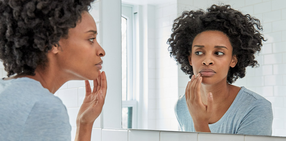 Woman standing in front of the mirror and applying Abreva cream 